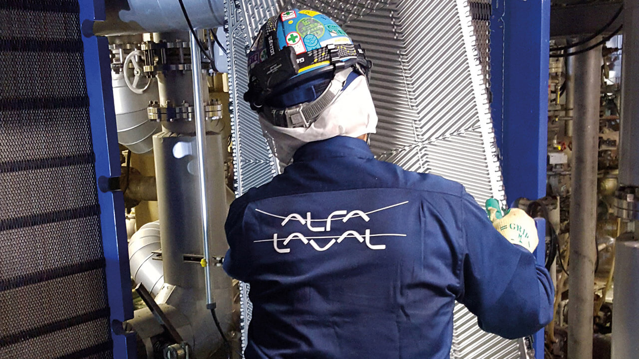 Industrial worker wearing protective gear servicing an Alfa Laval plate heat exchanger in a technical facility.